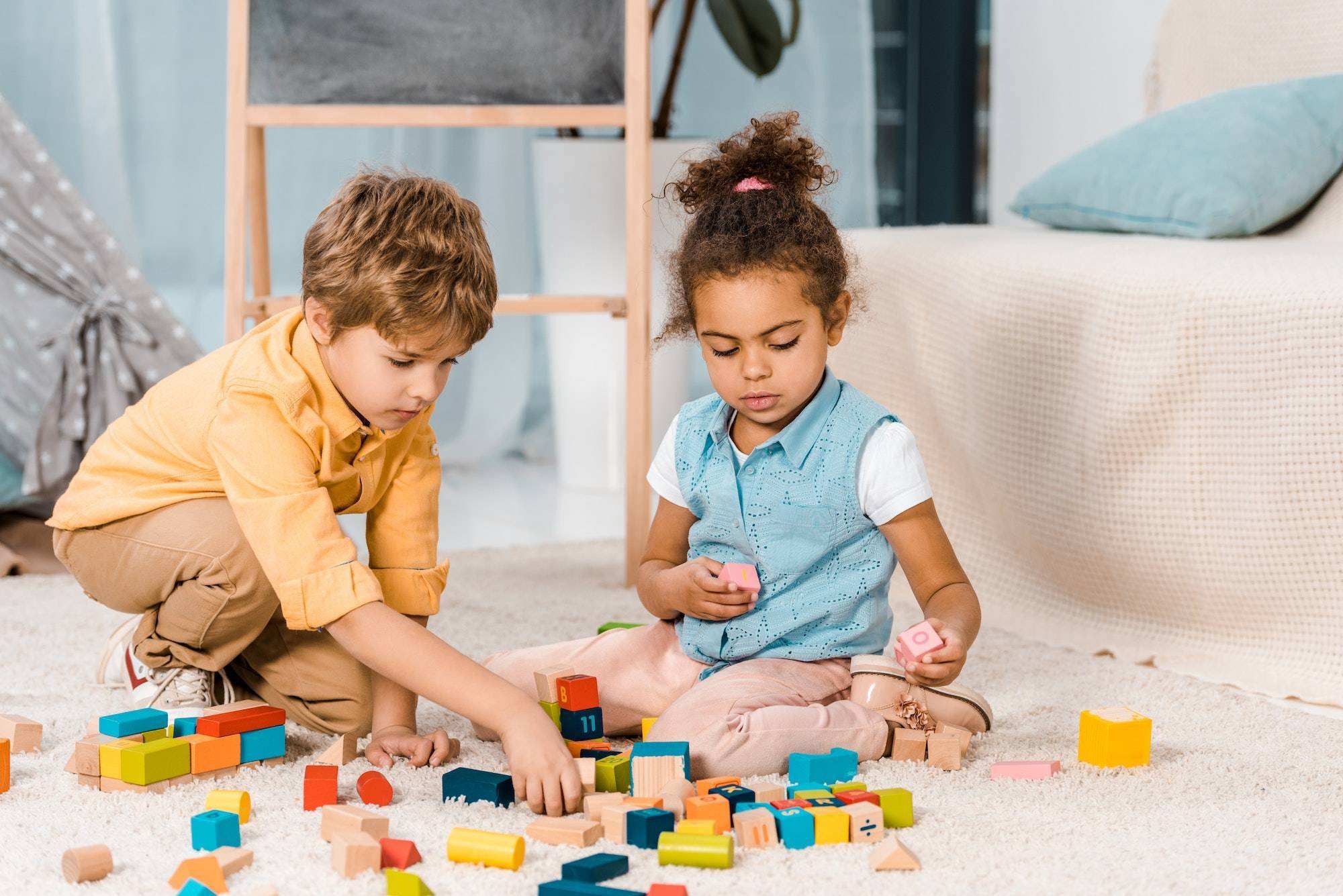 adorable multiethnic kids playing with colorful wooden blocks on carpet